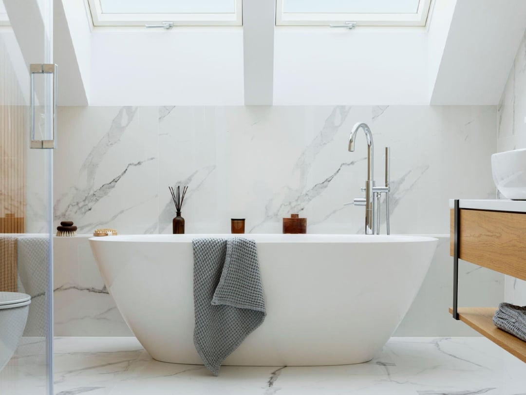 Freestanding bathtub with towels and bath oils in a marble bathroom
